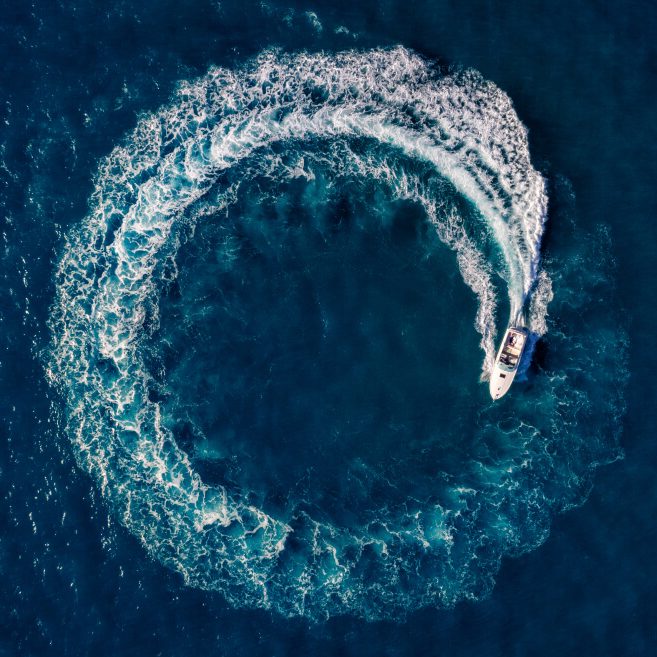 a white boat circles in the water, creating a circle shaped wave behind it